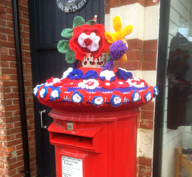 A red post box adorned with red white and blue 'flowers' and topped with a crown.